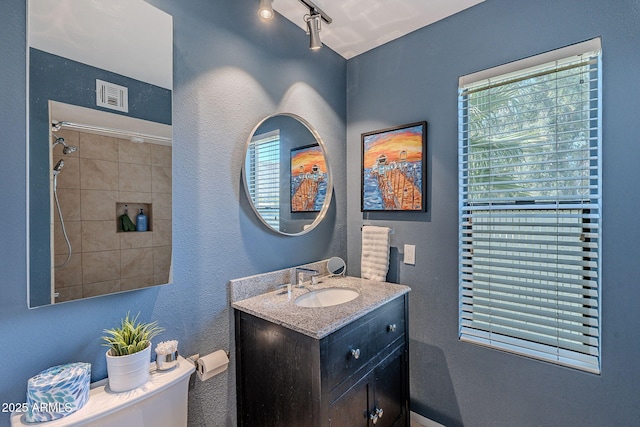 bathroom featuring vanity, tiled shower, a wealth of natural light, and toilet