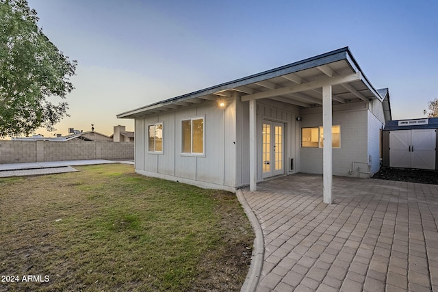 back house at dusk featuring a yard, a patio, and a storage unit