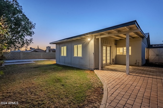 back house at dusk with a lawn, a patio area, and french doors