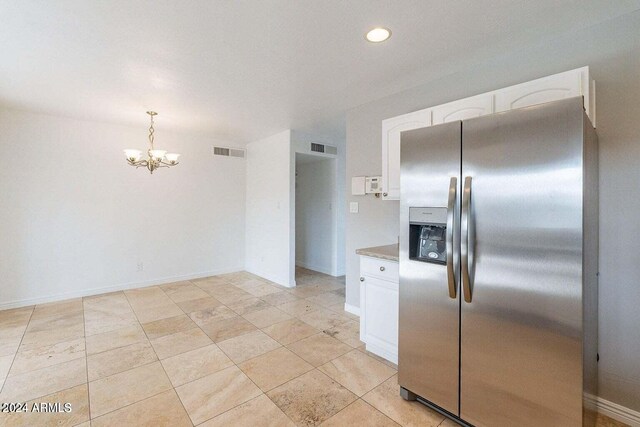 kitchen with white cabinets, stainless steel fridge, an inviting chandelier, and pendant lighting