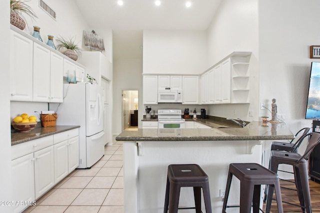 kitchen with white appliances, kitchen peninsula, white cabinets, and a towering ceiling