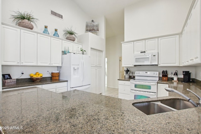 kitchen with sink, high vaulted ceiling, white appliances, dark stone counters, and white cabinets