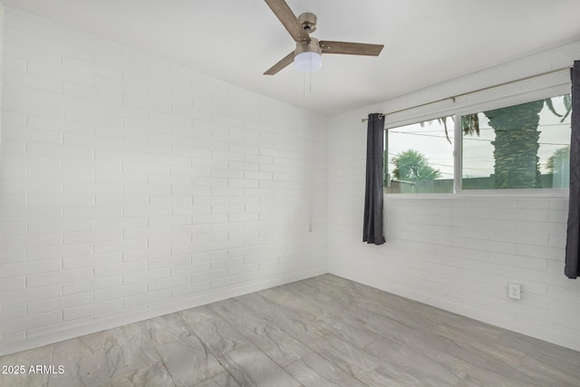 empty room featuring ceiling fan and brick wall