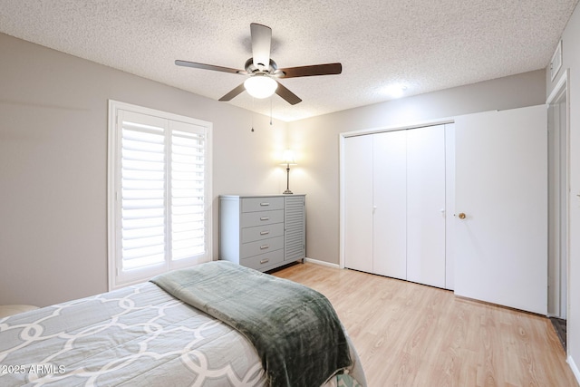 bedroom with ceiling fan, light wood-type flooring, a textured ceiling, and a closet