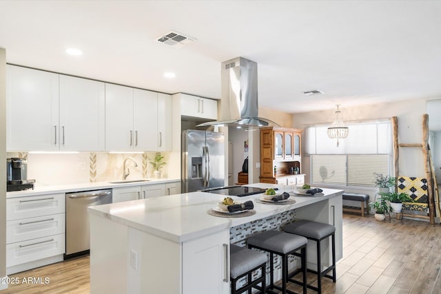 kitchen featuring white cabinetry, sink, island exhaust hood, a center island, and stainless steel appliances