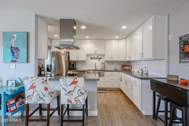 kitchen with sink, white cabinetry, a kitchen breakfast bar, stainless steel refrigerator with ice dispenser, and island exhaust hood