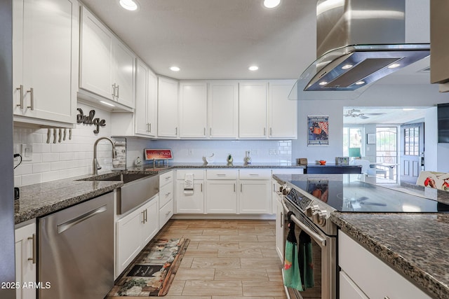 kitchen featuring appliances with stainless steel finishes, white cabinetry, sink, dark stone countertops, and island exhaust hood