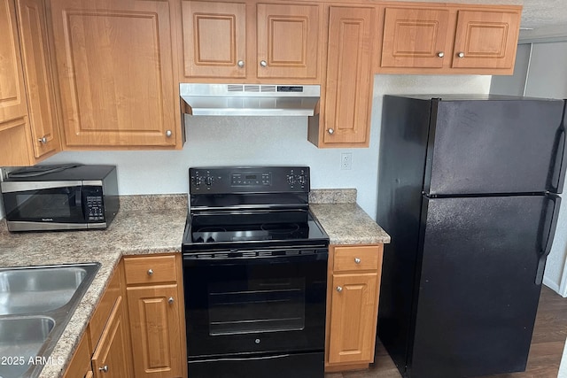 kitchen featuring black appliances, wood finished floors, under cabinet range hood, and a sink