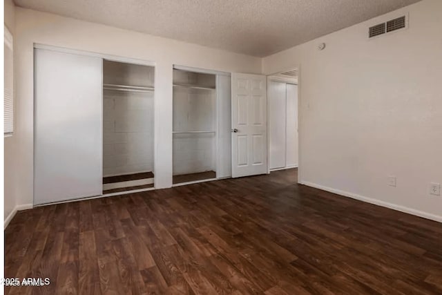 unfurnished bedroom with visible vents, multiple closets, a textured ceiling, and dark wood-style floors