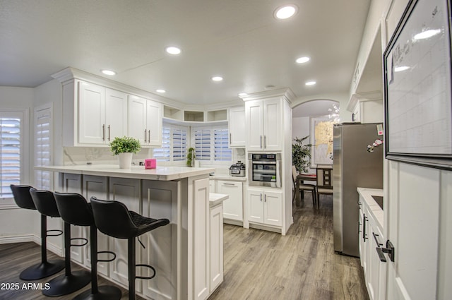 kitchen with a breakfast bar, decorative backsplash, light wood-type flooring, stainless steel appliances, and white cabinets