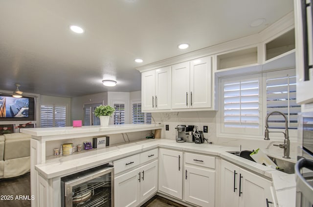 kitchen with kitchen peninsula, beverage cooler, white cabinets, light stone counters, and sink