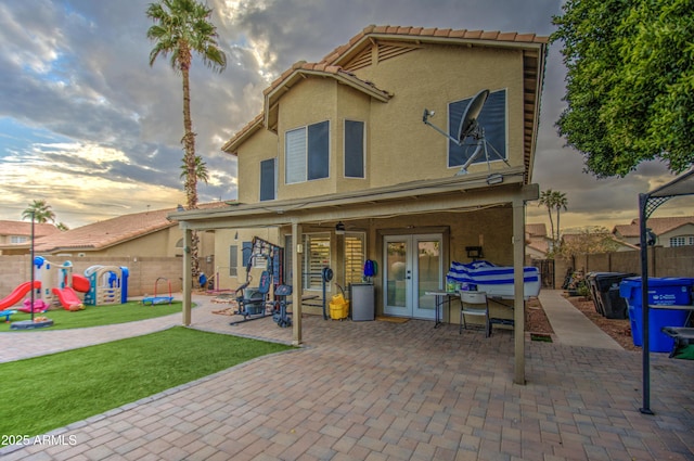 back house at dusk with a playground, a patio area, and french doors