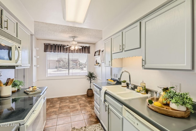 kitchen featuring a textured ceiling, white microwave, a sink, a ceiling fan, and baseboards