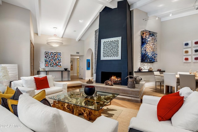 living room with light hardwood / wood-style flooring, beamed ceiling, a high ceiling, and a fireplace