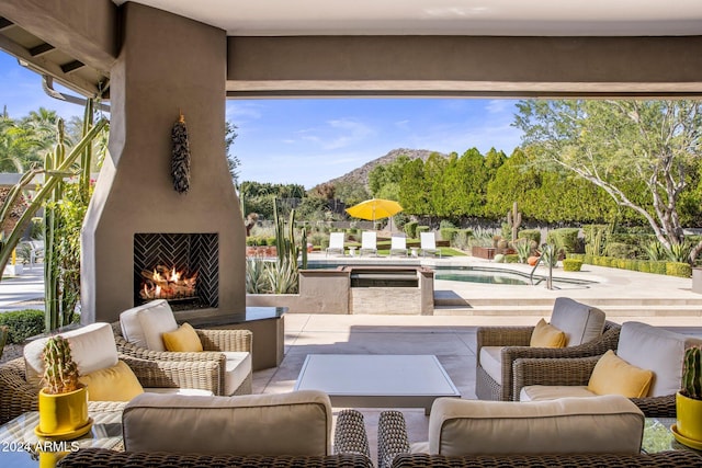 view of patio / terrace with a swimming pool with hot tub, an outdoor living space with a fireplace, and a mountain view