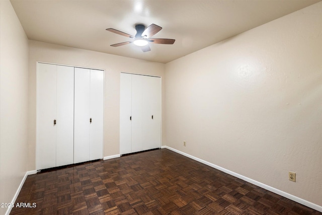 unfurnished bedroom featuring multiple closets, ceiling fan, and dark parquet flooring