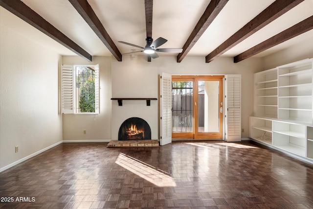 unfurnished living room with a warm lit fireplace, beam ceiling, a ceiling fan, and baseboards