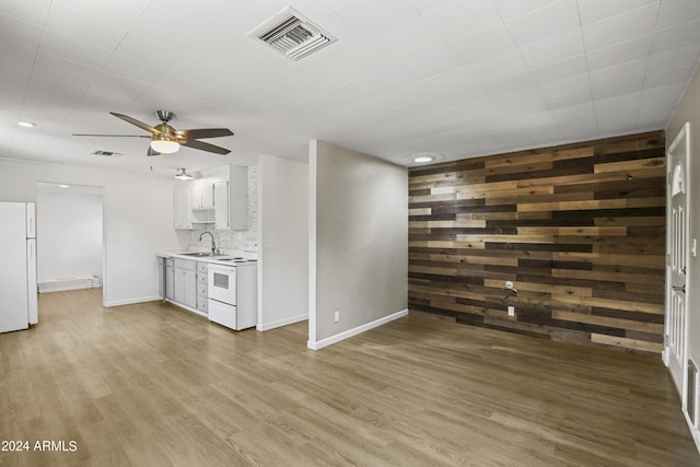 unfurnished living room with wooden walls, sink, ceiling fan, and light wood-type flooring