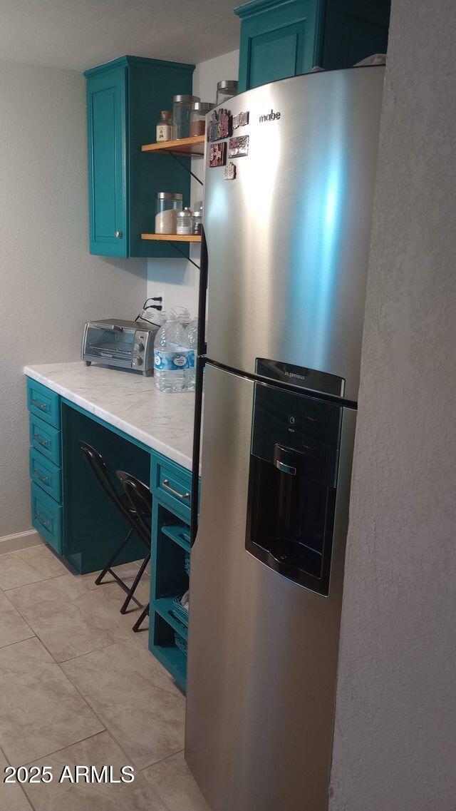 735 E 3rd St, Douglas, AZ 85608 - kitchen with stainless steel refrigerator with ice dispenser, open shelves, blue cabinets, light countertops, and a textured wall