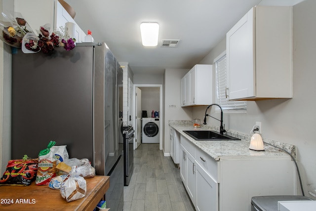 kitchen featuring light stone countertops, sink, white cabinetry, washer / clothes dryer, and light wood-type flooring