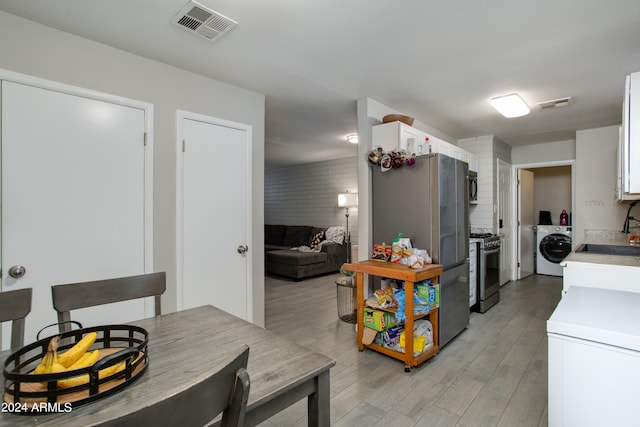 kitchen with appliances with stainless steel finishes, washer / clothes dryer, white cabinets, light hardwood / wood-style flooring, and sink