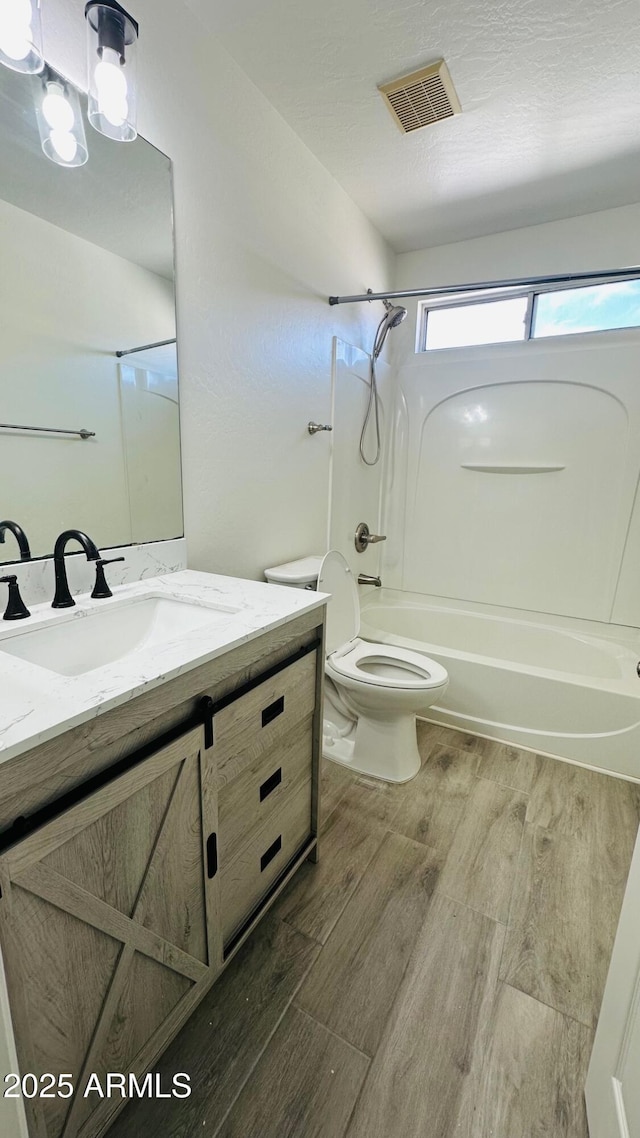 bathroom with shower / tub combination, toilet, wood finished floors, vanity, and visible vents