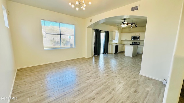 unfurnished living room featuring light wood-type flooring, arched walkways, a sink, and ceiling fan with notable chandelier