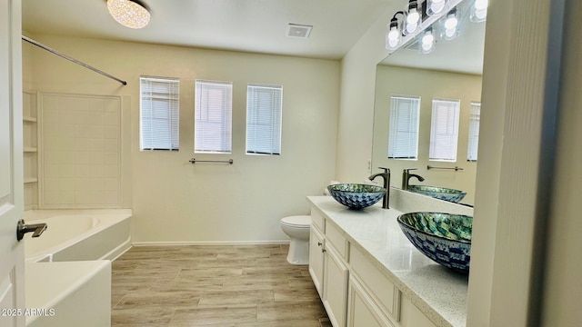 bathroom featuring double vanity, visible vents, a sink, wood finished floors, and baseboards