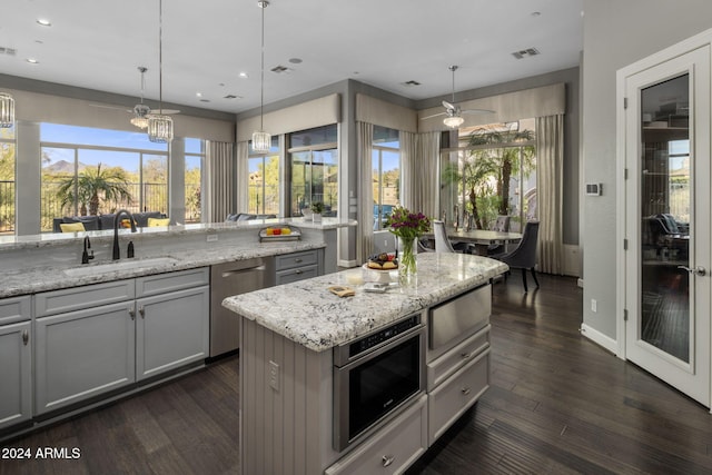 kitchen with light stone counters, appliances with stainless steel finishes, gray cabinets, pendant lighting, and sink