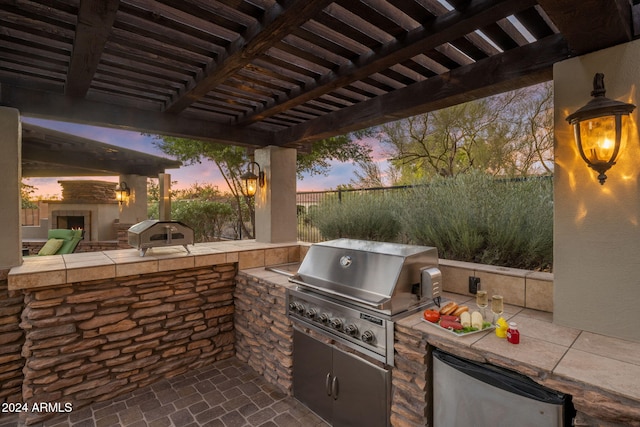 patio terrace at dusk with exterior kitchen, a pergola, and area for grilling