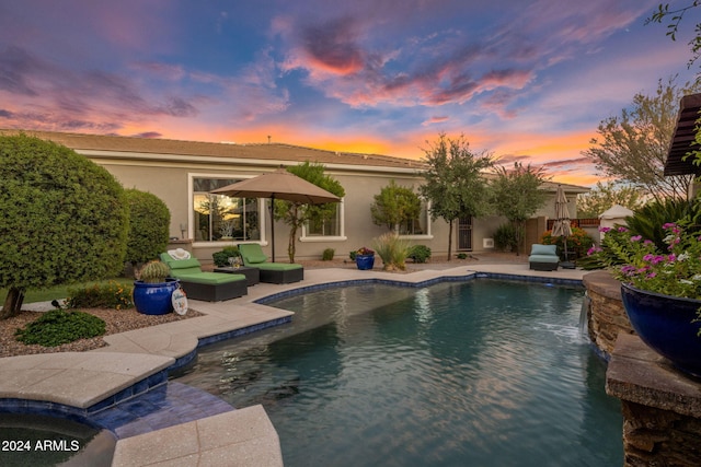 pool at dusk featuring an outdoor hangout area, pool water feature, and a patio area