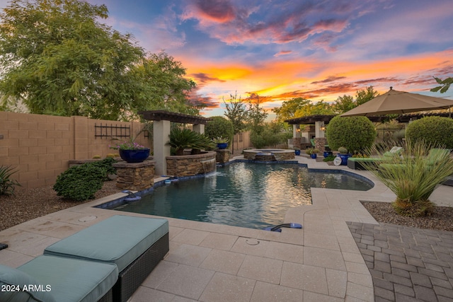 pool at dusk featuring pool water feature, a patio, and an in ground hot tub