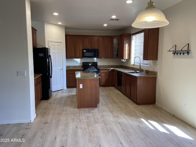 kitchen featuring visible vents, black appliances, a sink, a kitchen island, and glass insert cabinets