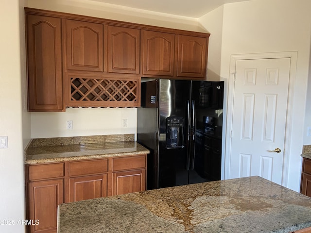 kitchen featuring stone countertops, brown cabinets, and black fridge