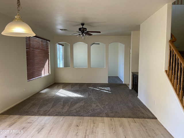 unfurnished room featuring visible vents, ceiling fan, stairway, wood finished floors, and arched walkways