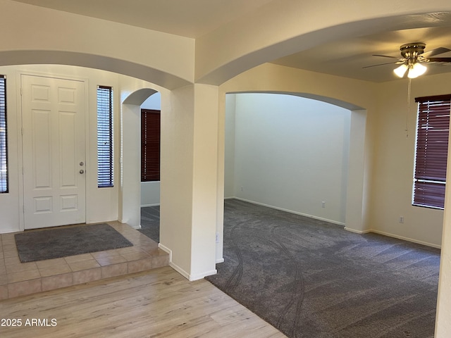 entryway featuring carpet, a ceiling fan, arched walkways, and baseboards