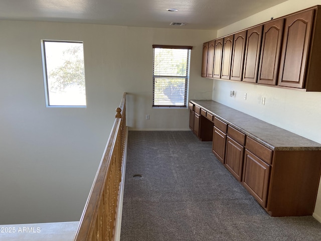 kitchen with dark countertops, visible vents, baseboards, dark carpet, and built in study area