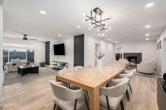 dining room featuring light wood-type flooring, ceiling fan, a fireplace, and recessed lighting