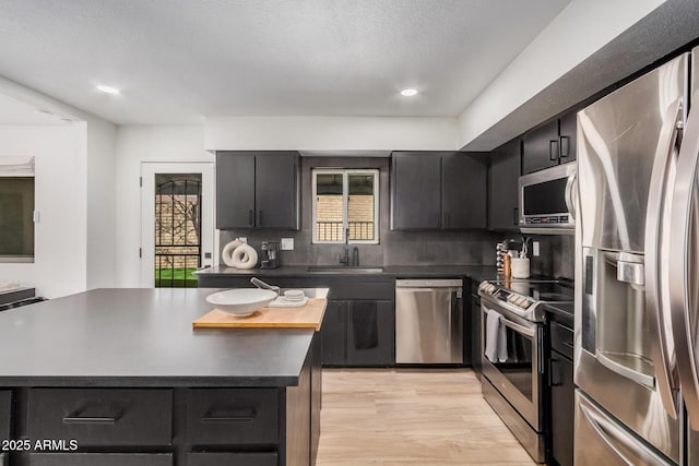 kitchen featuring a kitchen island, a sink, appliances with stainless steel finishes, light wood-type flooring, and dark countertops