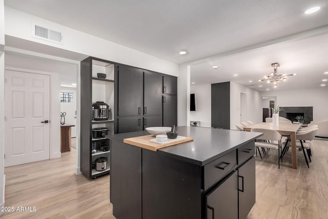 kitchen with light wood finished floors, visible vents, and dark cabinets