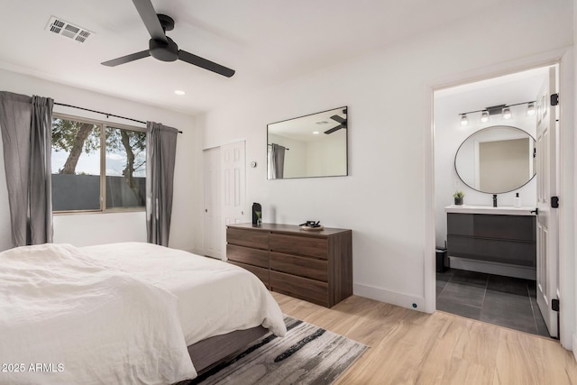 bedroom with ensuite bathroom, ceiling fan, visible vents, baseboards, and light wood finished floors