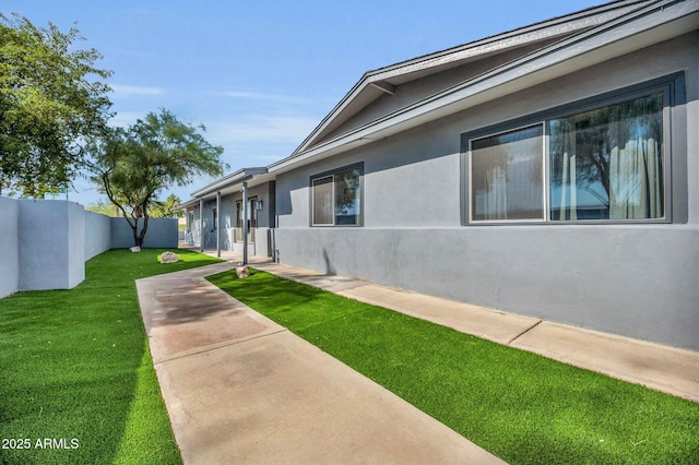 view of home's exterior featuring fence, a lawn, and stucco siding