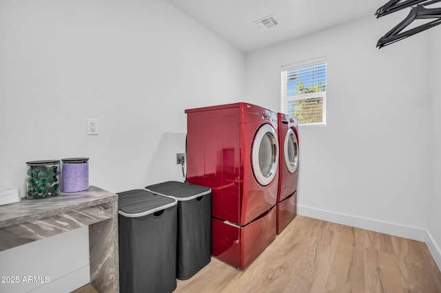 laundry area with light wood-style flooring, laundry area, visible vents, baseboards, and washing machine and clothes dryer