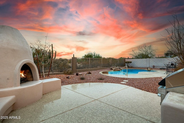 pool at dusk featuring an outdoor fireplace and a patio