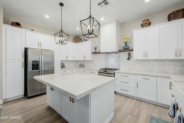 kitchen featuring pendant lighting, appliances with stainless steel finishes, white cabinetry, a center island, and wall chimney exhaust hood