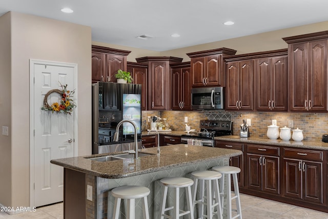 kitchen featuring appliances with stainless steel finishes, a kitchen bar, dark brown cabinets, a kitchen island with sink, and sink