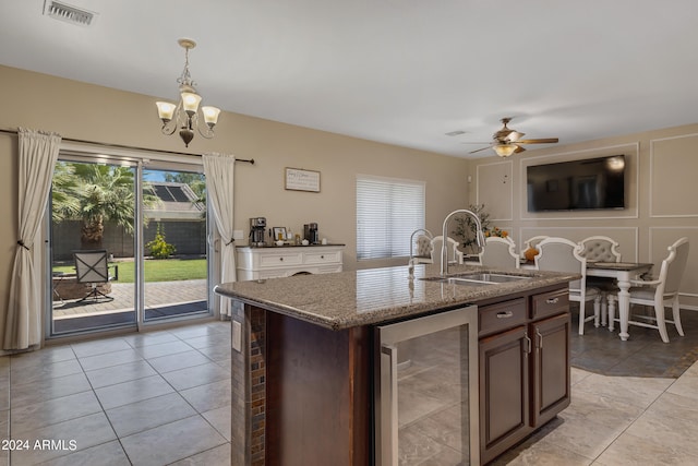 kitchen featuring ceiling fan with notable chandelier, pendant lighting, beverage cooler, dark brown cabinetry, and sink