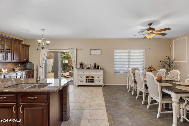 kitchen with pendant lighting, sink, dark stone counters, ceiling fan with notable chandelier, and decorative backsplash