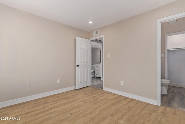 unfurnished bedroom with a closet, ensuite bathroom, light hardwood / wood-style flooring, and a spacious closet