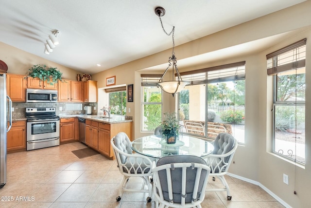 kitchen featuring lofted ceiling, a sink, hanging light fixtures, appliances with stainless steel finishes, and light stone countertops